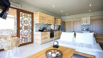 A modern kitchen with wooden cabinets and a stone backsplash, a dining area with a wooden table and chairs, and a bedroom with a large bed and white bedding.