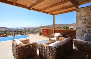 A covered outdoor area with wicker furniture, a stone wall, and a view of the landscape.