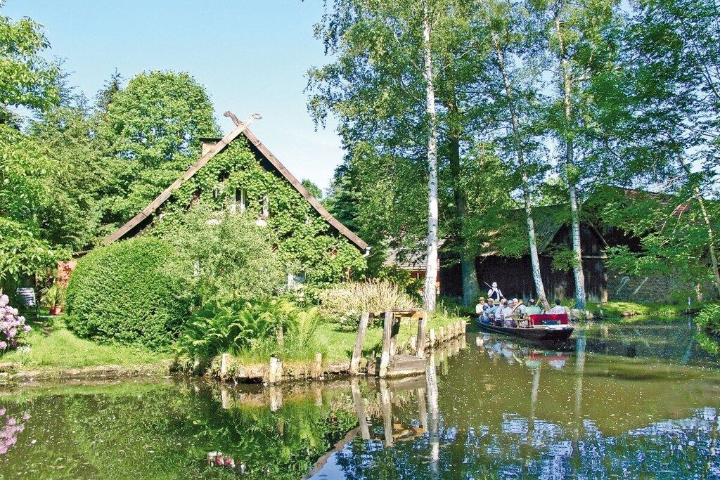 A boat on a calm river with a house covered in greenery on the left.