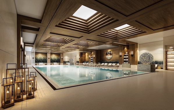 Une vaste piscine intérieure dotée de poutres en bois au plafond, d’espaces de détente et d’un éclairage moderne.