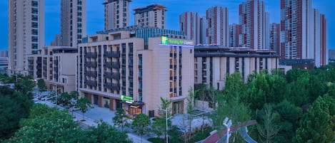 A multi-story hotel with a prominent Holiday Inn Express sign, surrounded by high-rise buildings and lush greenery.