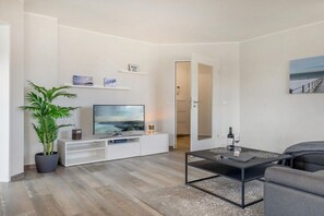 A modern living room with a flat-screen TV, a potted plant, a coffee table, and a grey sofa. - Granitz Residential Park 26 Sandschloss (Ostseebad Binz)