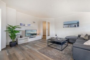 Een moderne woonkamer met een flatscreen televisie, een salontafel, een grijze bank en een potplant.