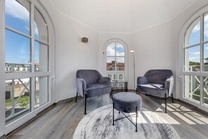 A room with two armchairs, a small round table, and a large window with a view of buildings. - Granitz Residential Park 26 Sandschloss (Ostseebad Binz)