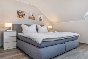 A modern bedroom with a grey bed, white pillows, and a nightstand with a lamp. - Granitz Residential Park 26 Sandschloss (Ostseebad Binz)