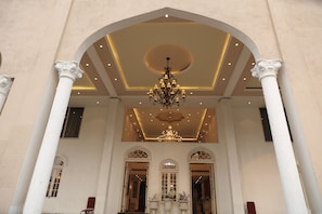 Un lobby espacioso con techo alto, columnas ornamentales y un candelabro.