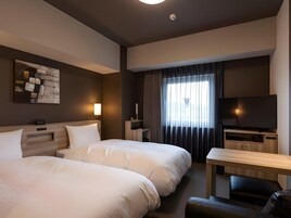 Habitación de hotel con dos camas, televisión, escritorio y un ventanal con cortinas.