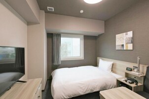 Una habitación de hotel con cama, mesita de noche, despertador y televisor.