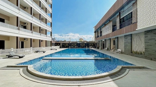 Una piscina con un centro azul cristalino, rodeada por un edificio de varios pisos con balcones y una fachada decorada.