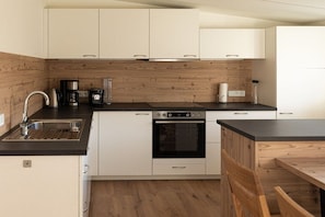 Eine moderne Küche mit weißen Schränken, einer Holz-Spritzschutzwand, einer Edelstahl-Spüle, einer Kaffeemaschine und einem Backofen.