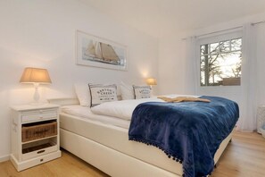Un dormitorio con una cama, dos mesitas de noche, una ventana y un cuadro en la pared.
