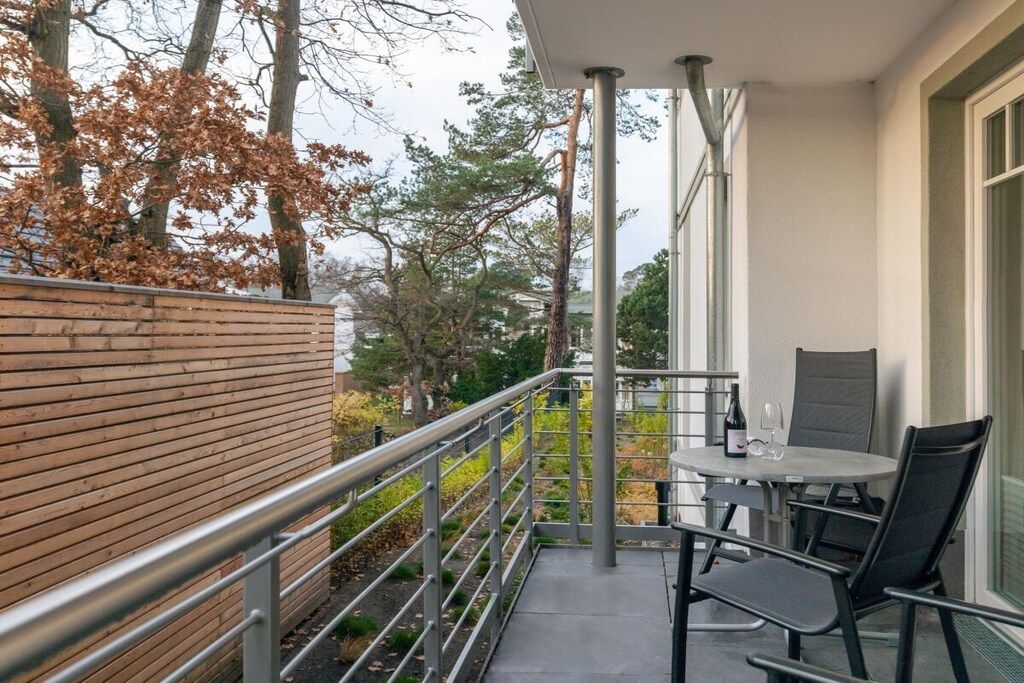 A balcony with a table and chairs, a bottle of wine, and a view of trees and buildings.