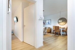 A modern interior with a wooden floor, a dining area with chairs and a table, and a wall-mounted clock. - Villa Düne 4 Summer retreat (Ostseebad Binz)