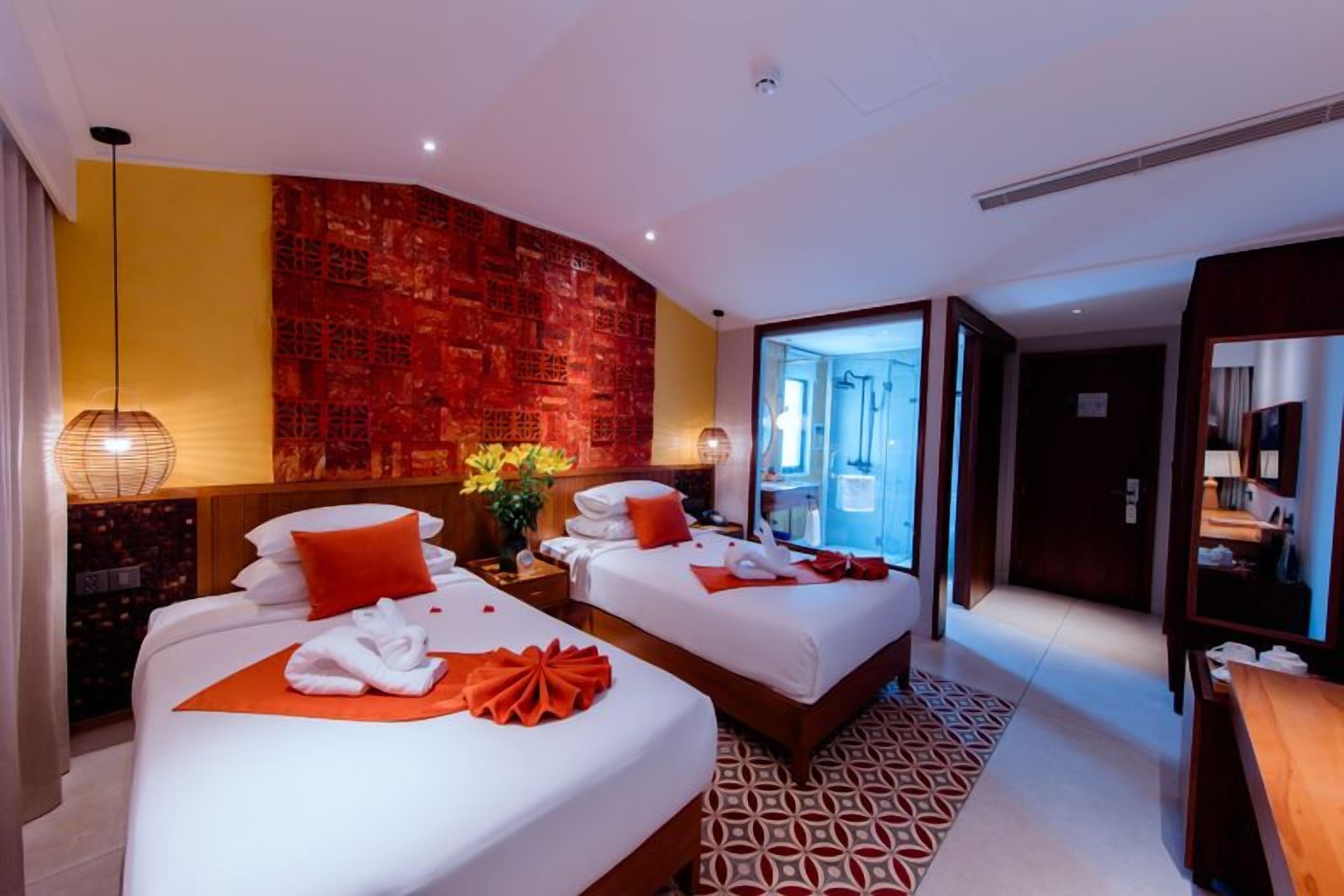 A hotel room with two beds, a red accent wall, a large window, and a modern design.