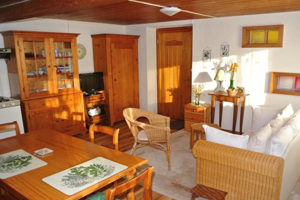 Ein gemütliches Wohnzimmer mit einem Holzesstisch, Korbstühlen, einer Couch und einem Fernseher.