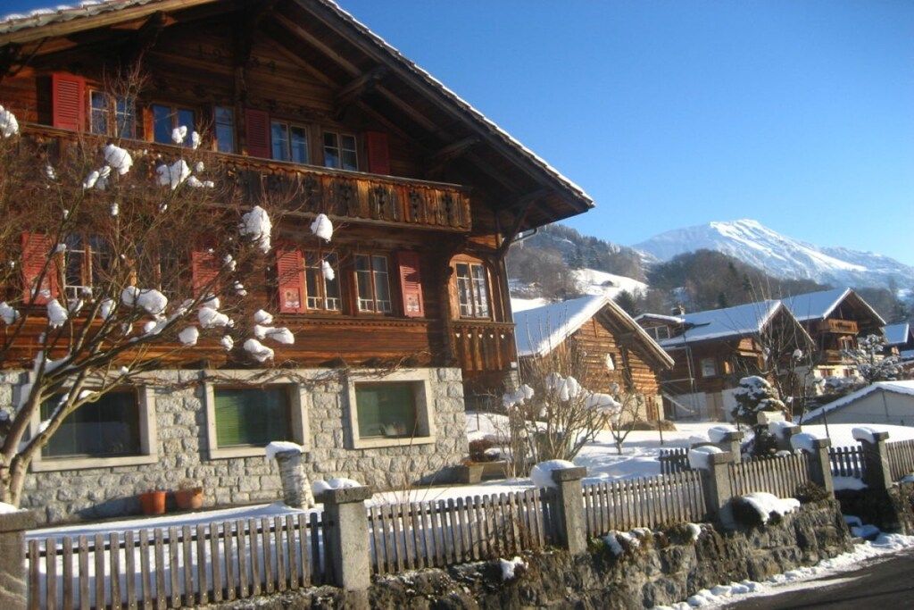 A wooden chalet with a stone facade, multiple windows, and a balcony.