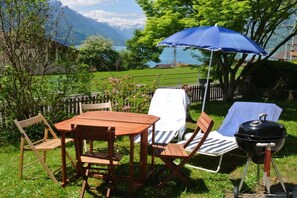 Ein Essbereich im Freien mit einem Holztisch, Stühlen, einem Grill und einem blauen Sonnenschirm.