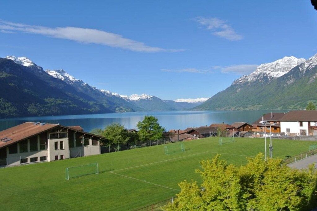 Ein Wohngebiet mit einer grünen Wiese, Häusern und Bergen im Hintergrund.