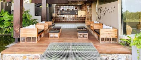 An outdoor seating area with wooden benches and tables, a woven ceiling light fixture, and a sign indicating a sustainable resort.