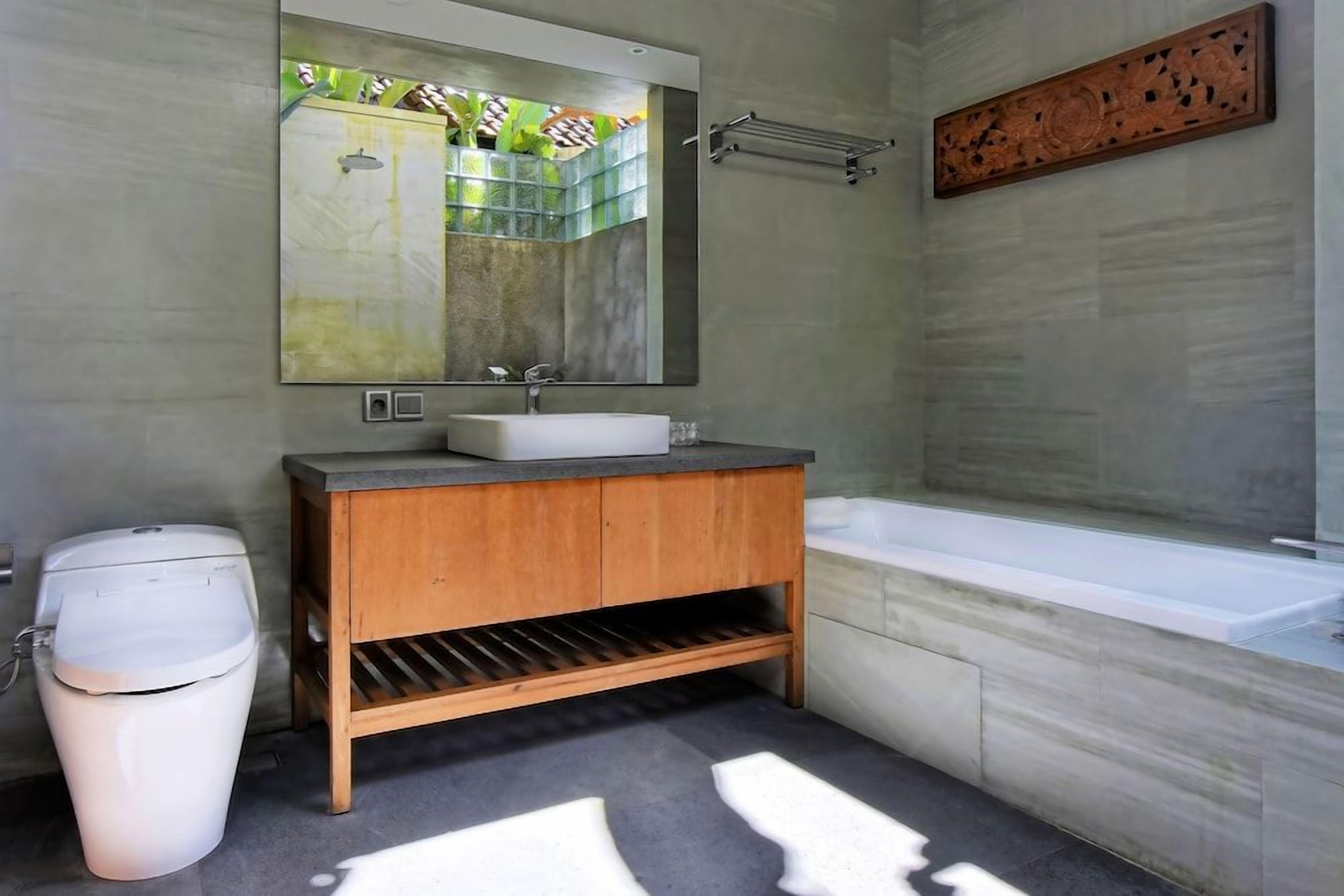 A bathroom with a wooden vanity, a white sink, a large mirror, and a bathtub.