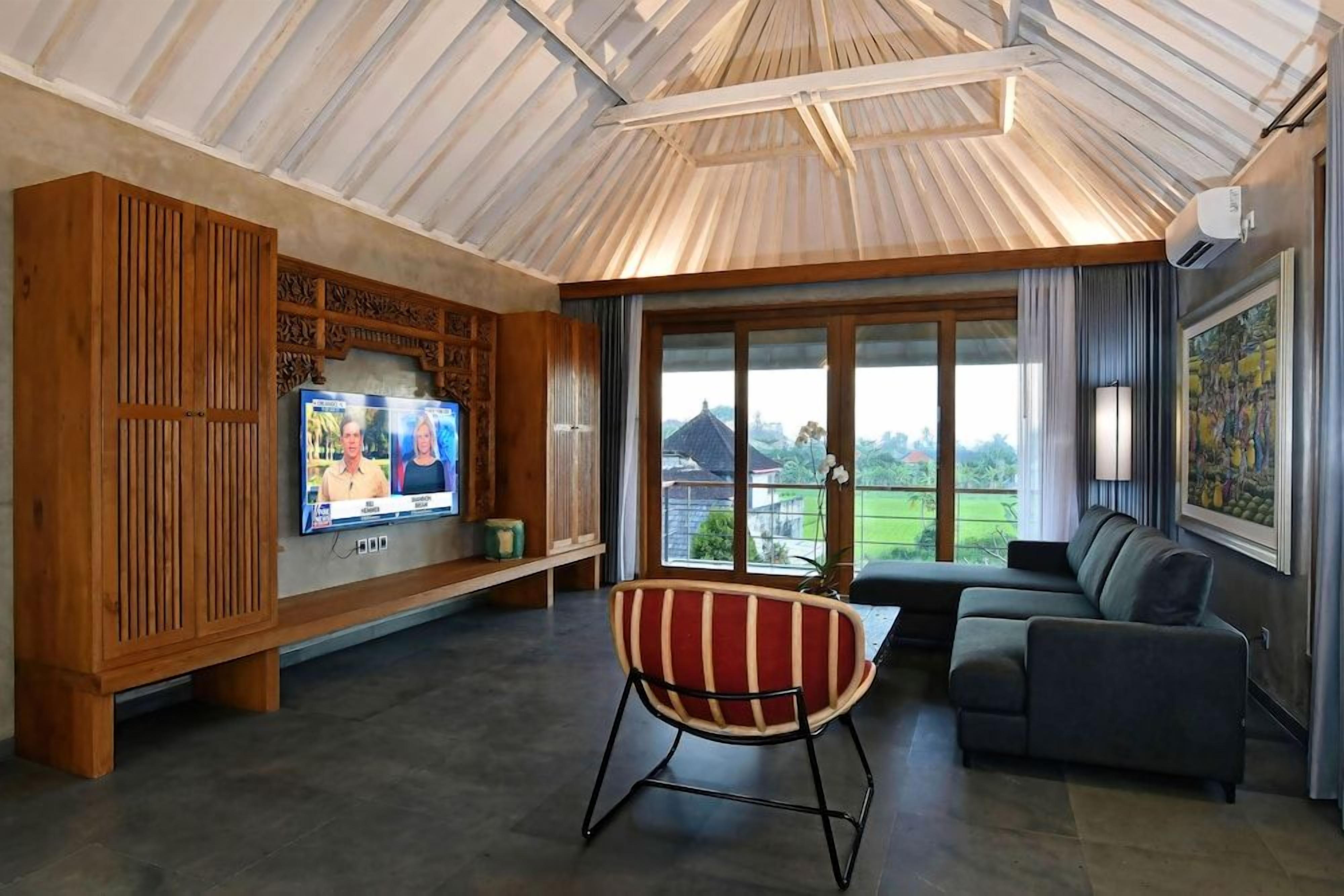 A living room with a television, a sofa, a chair, and a large window with a view of greenery.