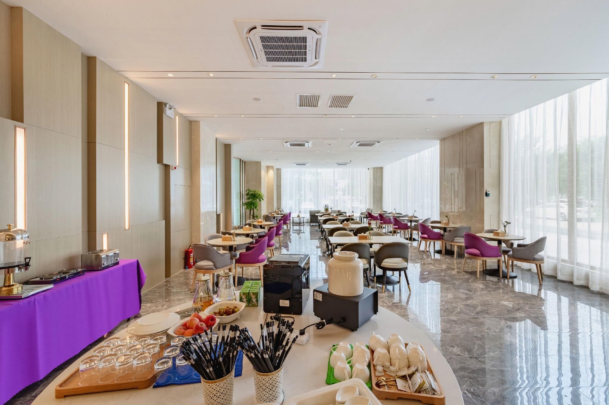 Ampla sala de jantar de hotel com várias mesas, cadeiras e um buffet.