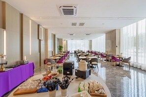 Ampla sala de jantar de hotel com várias mesas, cadeiras e um buffet.