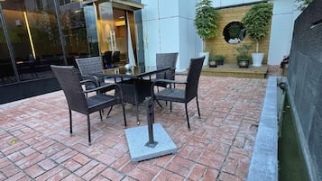 Um pátio externo com mesa e cadeiras, piso de tijolos e parede de vidro.