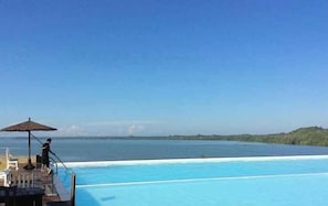 Piscina com vista para o mar e uma pessoa à beira da piscina.