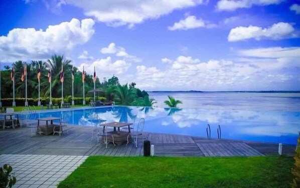 Área de piscina com deck de madeira, espreguiçadeiras e vista para a água.
