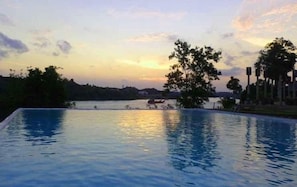 Piscina infinita com vista para um pôr do sol sobre a água.