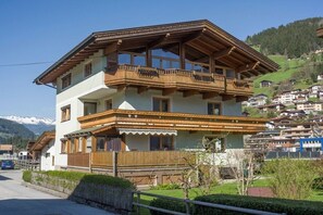 Ein zweistöckiges Gebäude mit Balkon, Holzfassade und Blick auf eine Berglandschaft.