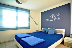 Ein Schlafzimmer mit einem Bett, Kissen, einem Nachttisch, einem Fenster und einem Wanddekor.