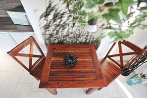 A wooden table with a central decorative piece, surrounded by chairs, in a room with a white floor and a plant in the background. - Holiday apartment with 1 bedroom (Graal-Müritz)