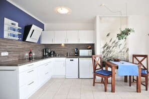 Eine moderne Küche mit weißen Schränken, einer Mikrowelle und einer Kaffeemaschine. Ein Esstisch mit Stühlen und einer blauen Tischdecke steht bereit.