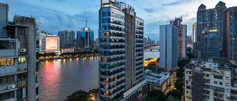 A high-rise building with a distinctive architectural feature near the top, surrounded by other modern buildings and a river.