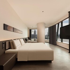 Habitación de hotel moderna con una cama grande, zona de estar, televisor y vistas a la ciudad.