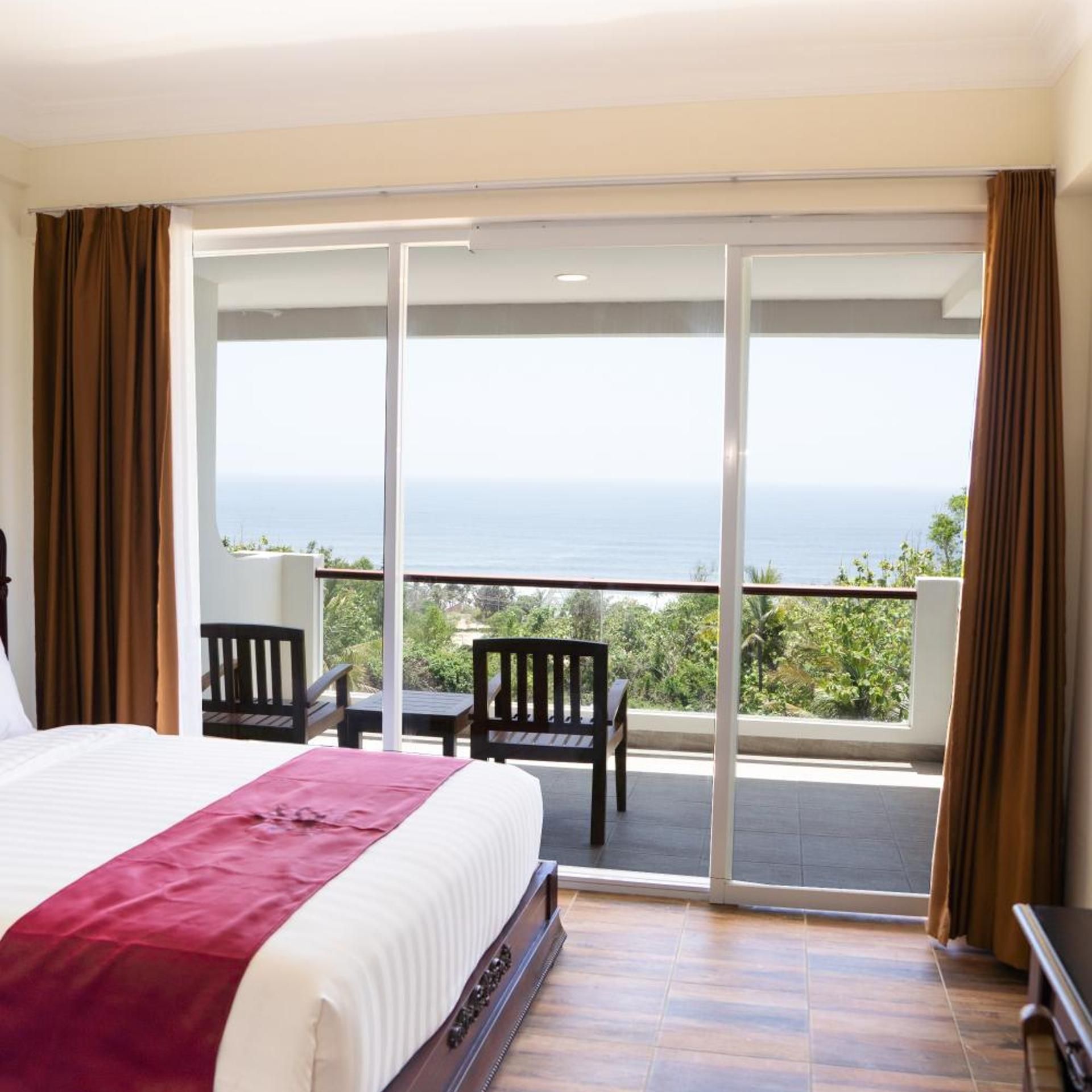 A hotel room with a bed, a balcony with a view of the sea, and two chairs.