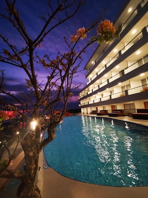 A hotel with a swimming pool, multiple balconies, and a tree with pink flowers. - D Girijati Resort and Beach Club (Parangtritis)