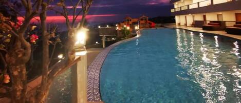 A swimming pool with a curved edge, surrounded by a building with multiple balconies.