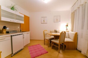 A compact kitchen with white cabinets, a small refrigerator, and a dining area with a wooden table and chairs. - Holiday home with 1 bedroom (8344 Bad Gleichenberg)