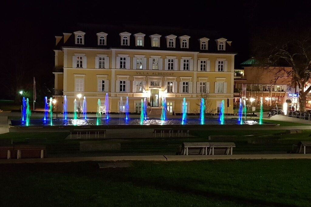 Ein Hotel mit Springbrunnen davor, einem gepflegten Rasen und klassischer Architektur.