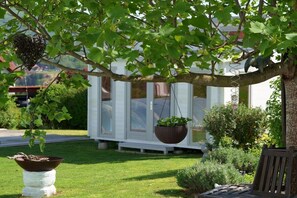 A tree with hanging planters and a bench in a well-maintained garden area. - Holiday home with 1 bedroom (8344 Bad Gleichenberg)