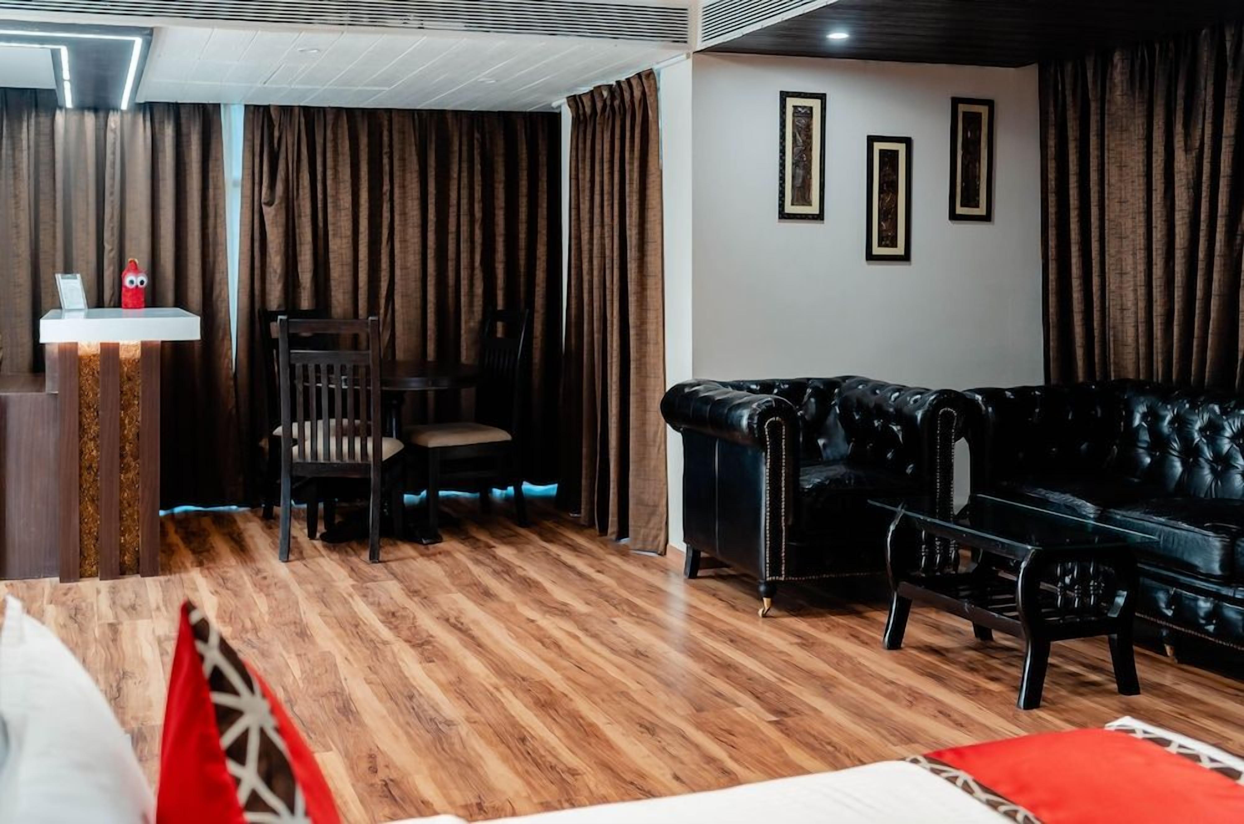A room with a black leather sofa, a wooden dining table with chairs, and a small white table with a red object on it.