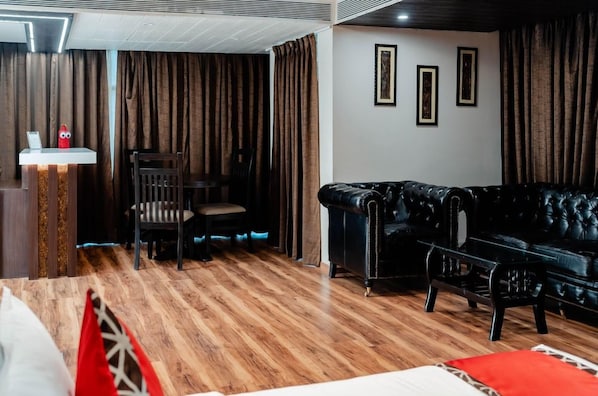A room with a black leather sofa, a wooden dining table with chairs, and a small white table with a red object on it.