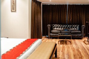 A hotel room with a bed, a bench, a sofa, and a large window with curtains.