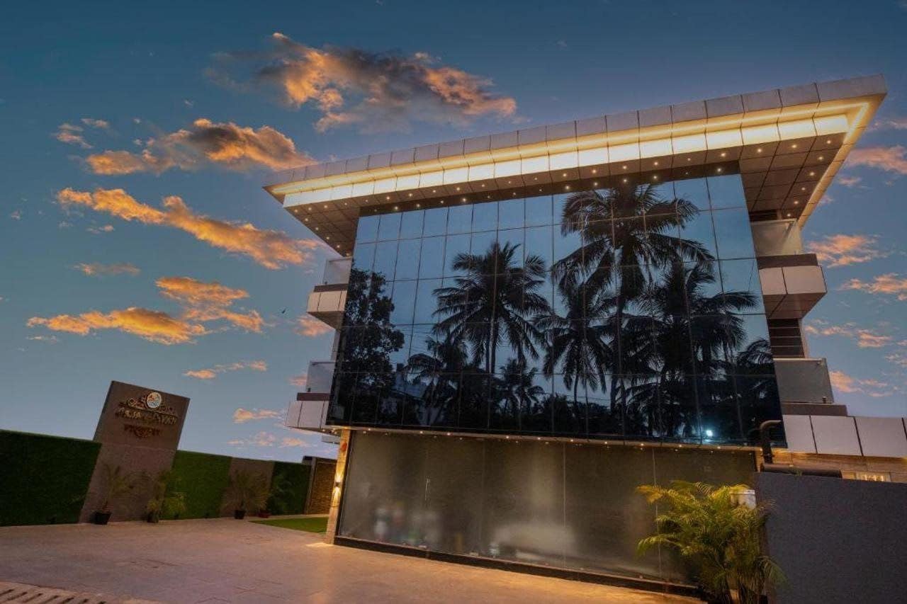A modern building with a glass facade reflecting palm trees, a covered walkway, and a sign with text.