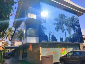 A modern building with a glass facade reflecting palm trees, a car parked in front, and a sign with 'Happy New Year' written on it.