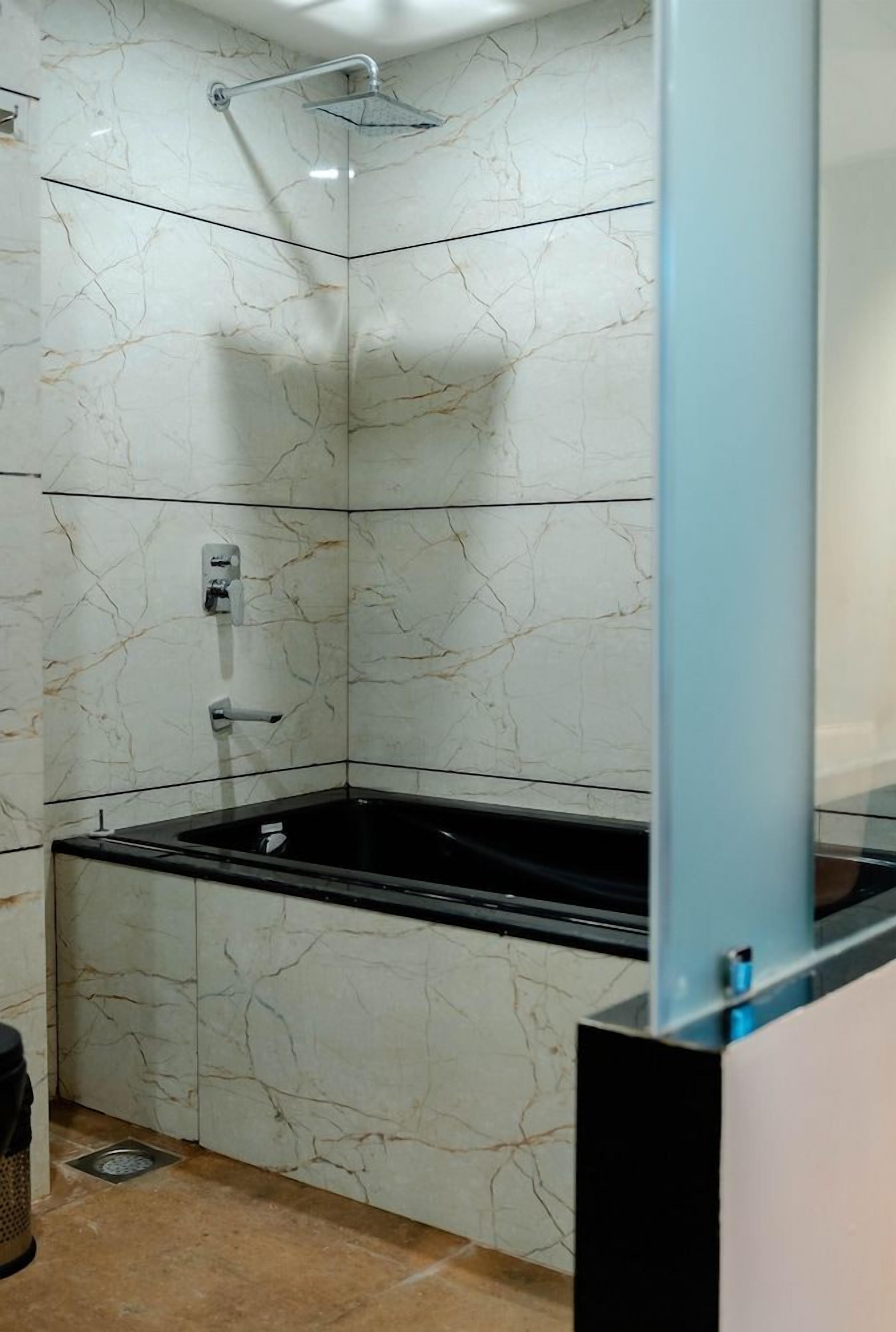 A corner shower with a glass enclosure, a black bathtub, and a marble wall.