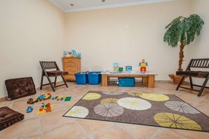 Quarto com área de recreação, incluindo brinquedos, uma mesa com livros e uma cadeira.